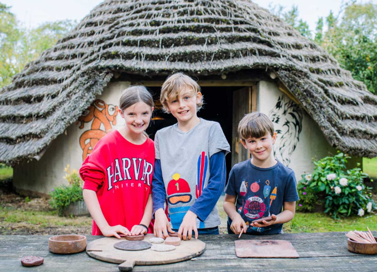 Children making Celtic jewellery out of clay in front of a historic settlement building